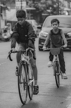 Two children riding bicycles on a street, captured in black and white, conveying freedom and adventure.