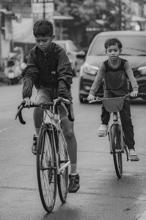 Free Two children riding bicycles on a street, captured in black and white, conveying freedom and adventure. Stock Photo