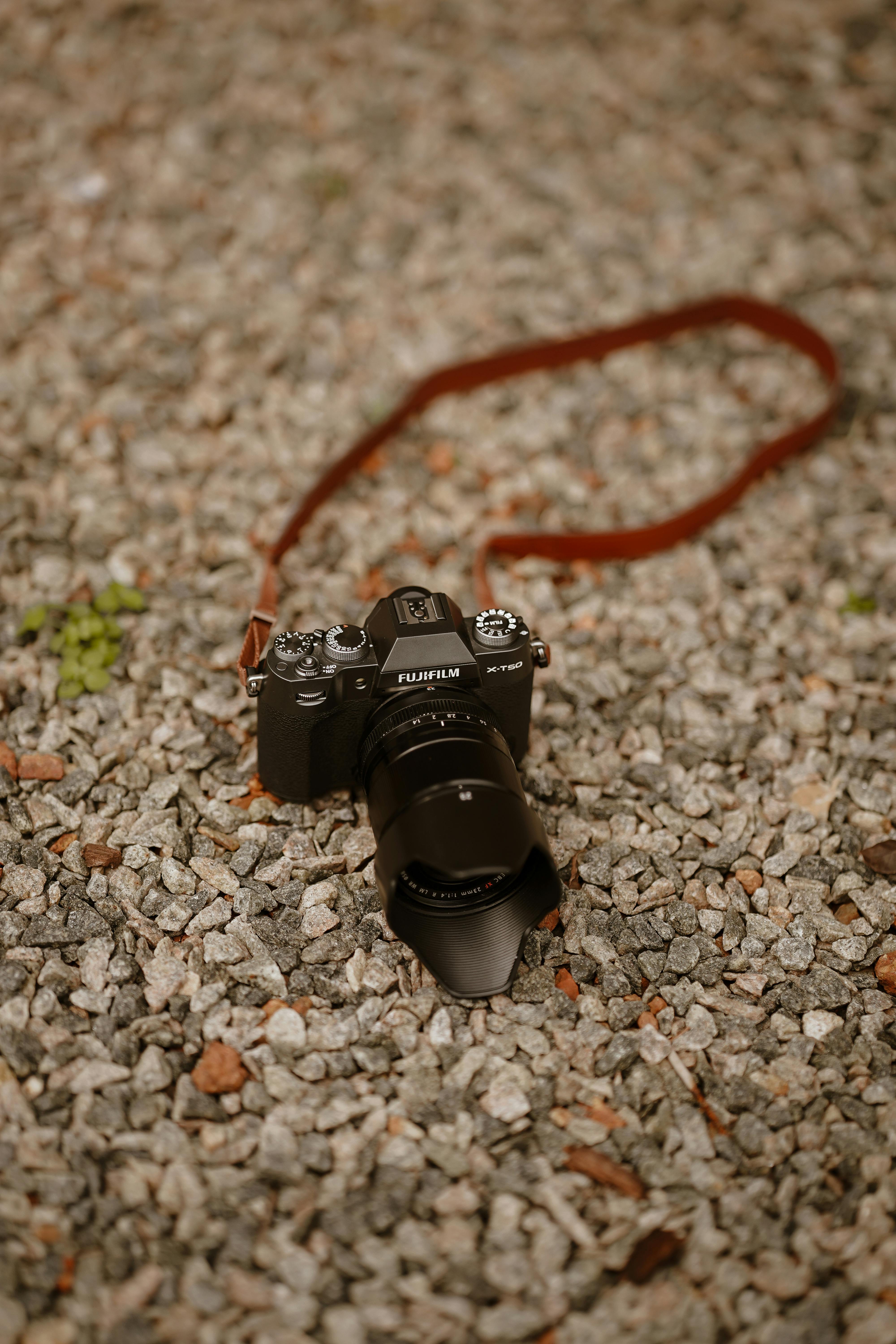 Free A DSLR camera with a brown strap on a gravel surface, in soft focus. Stock Photo