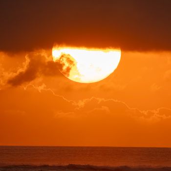 Stunning sunset view in Bali with sun partially hidden by clouds over the ocean.