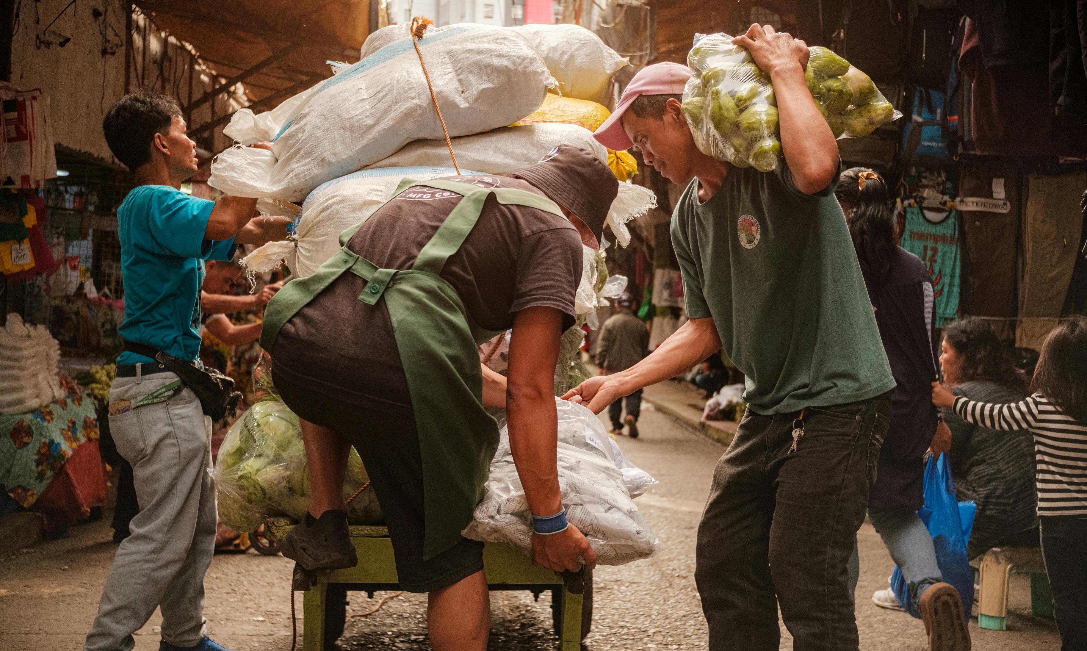 Gratis Trabajadores cargando un carro con productos en un bullicioso mercado callejero. Foto de stock