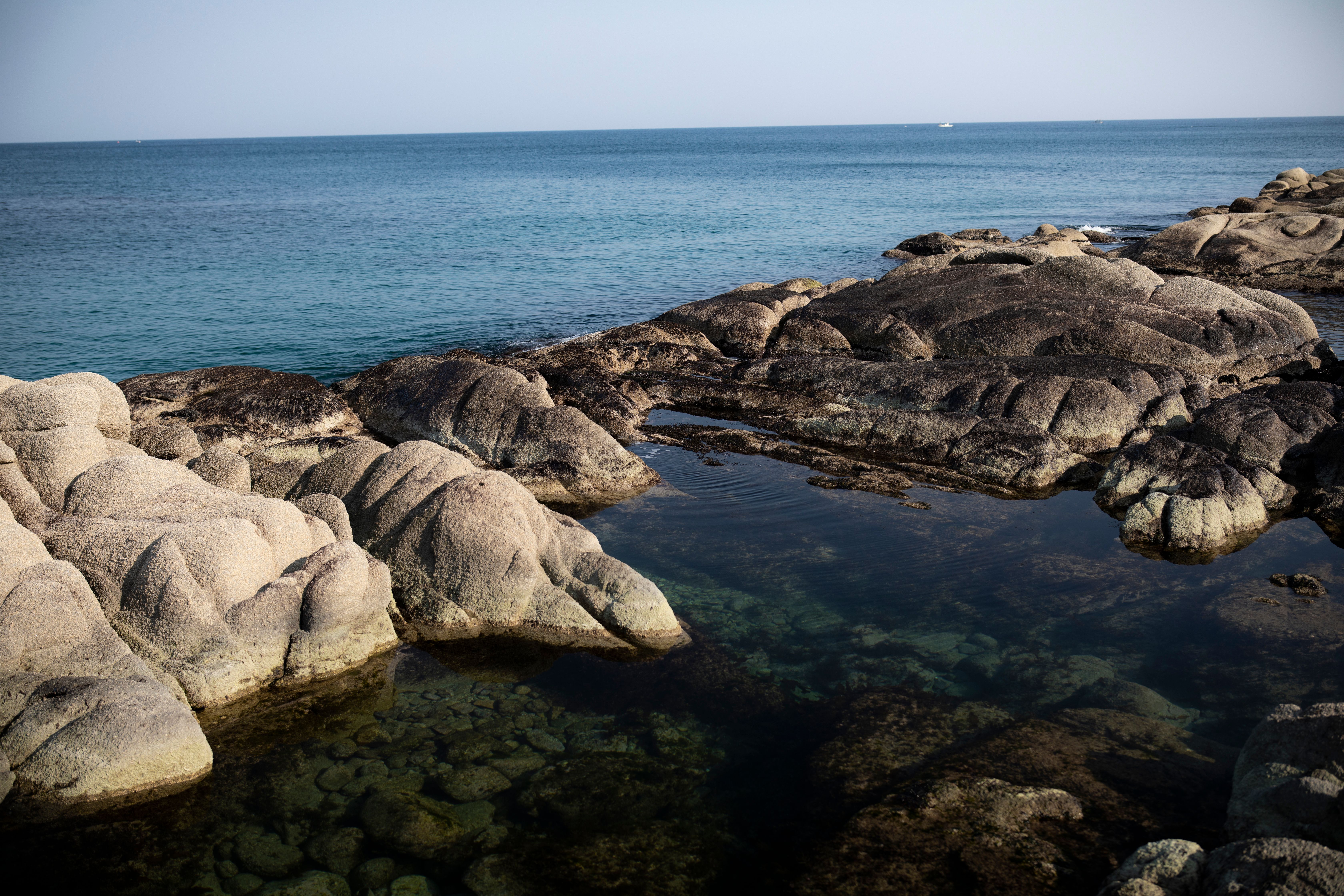 Natural rocky seashore with clear waters and a serene ocean view.