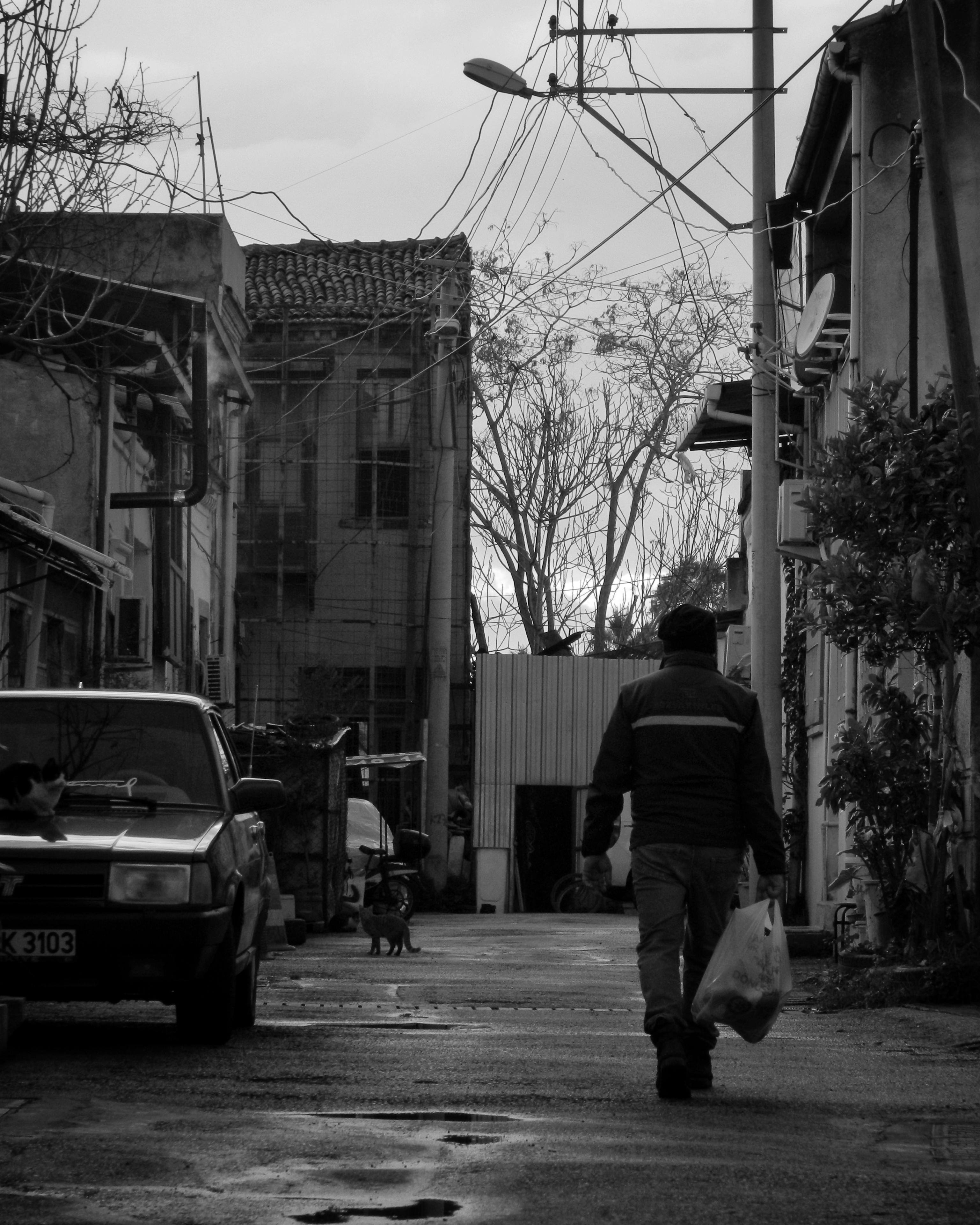 Free A man walking down an alleyway carrying bags in a moody black and white setting. Stock Photo