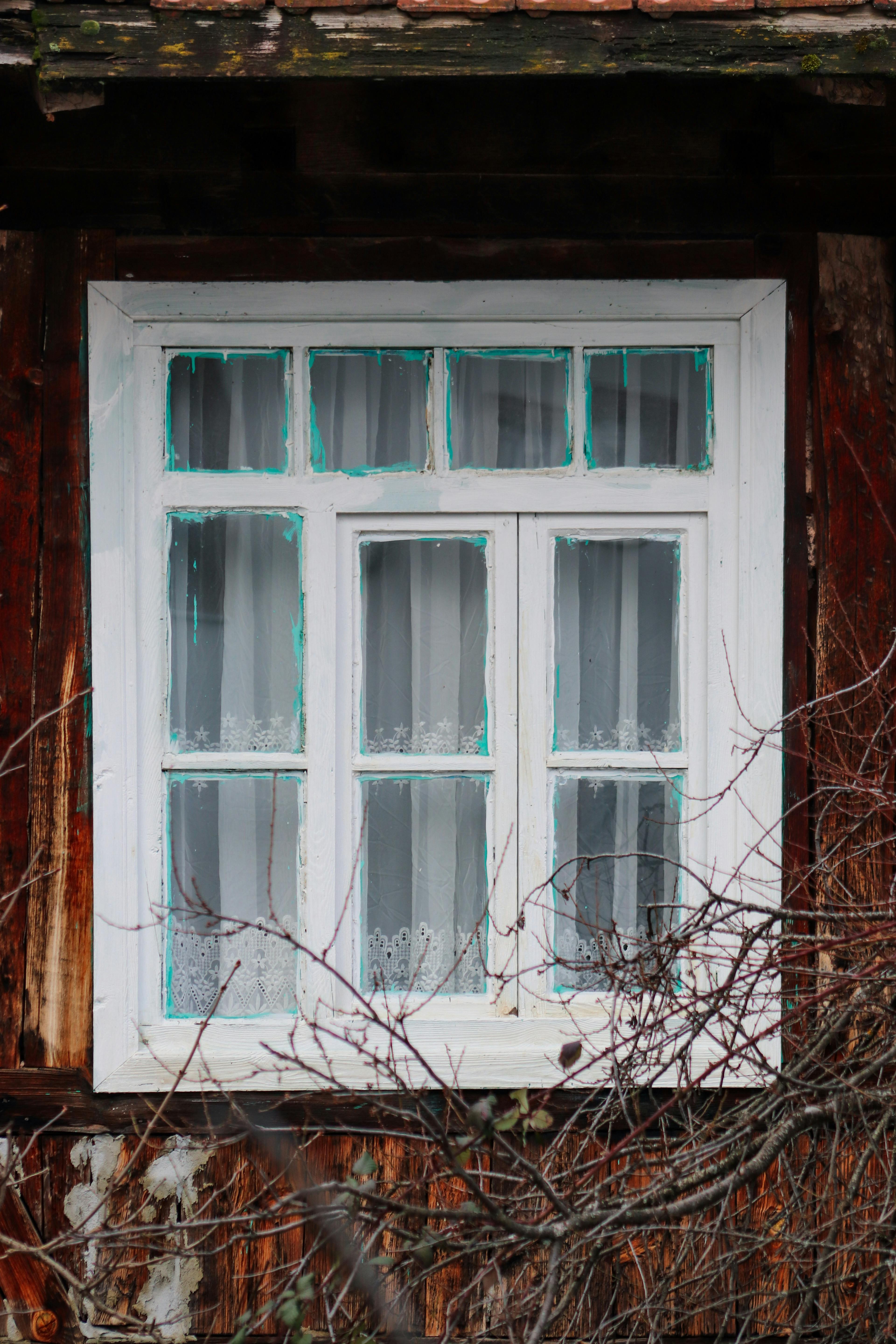 Gratis Una encantadora ventana de una casa rústica de madera enmarcada por intrincadas cortinas de encaje y madera desgastada. Foto de stock