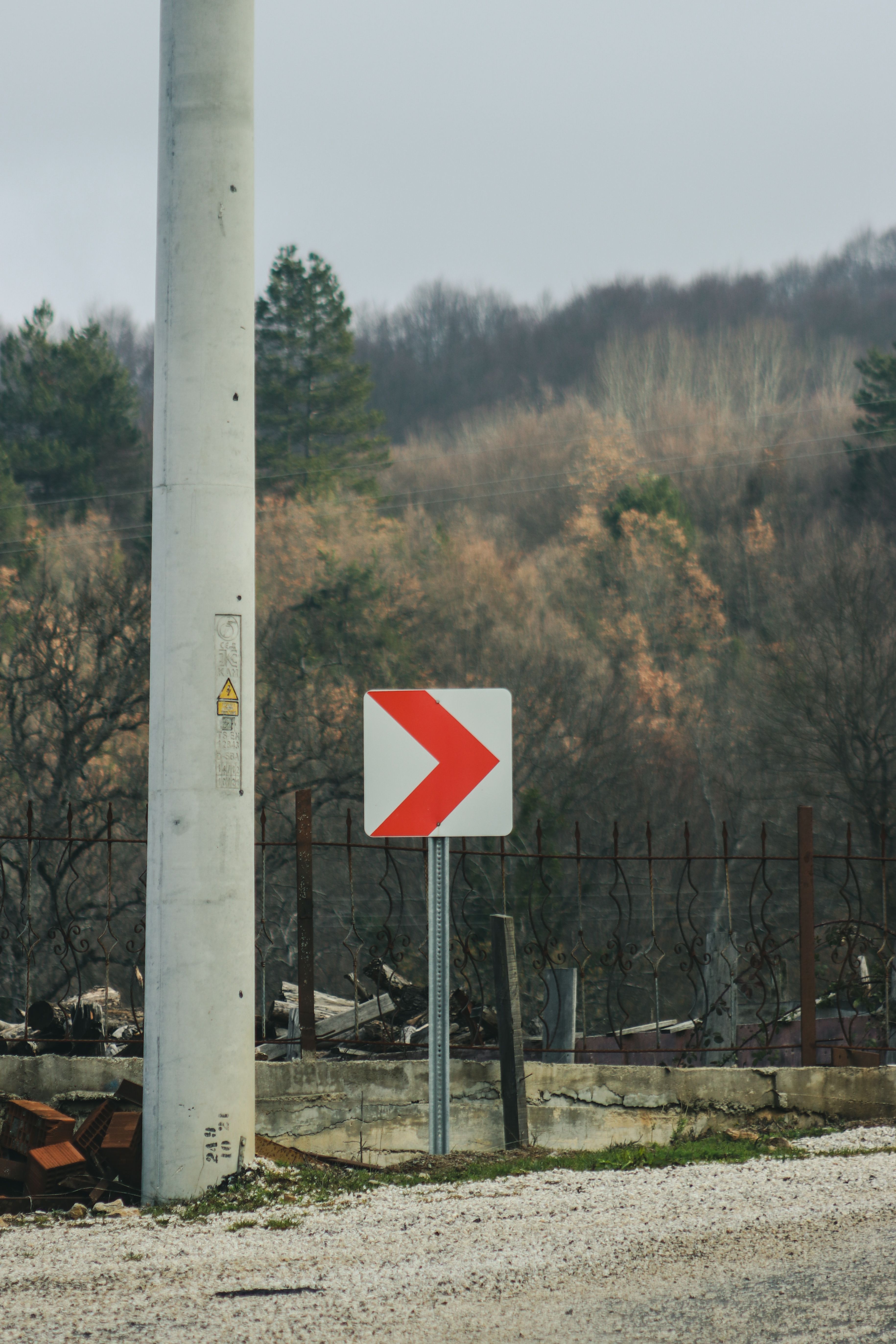 A rural roadside scene featuring a red arrow directional sign against a wooded backdrop, hinting at an approaching turn.