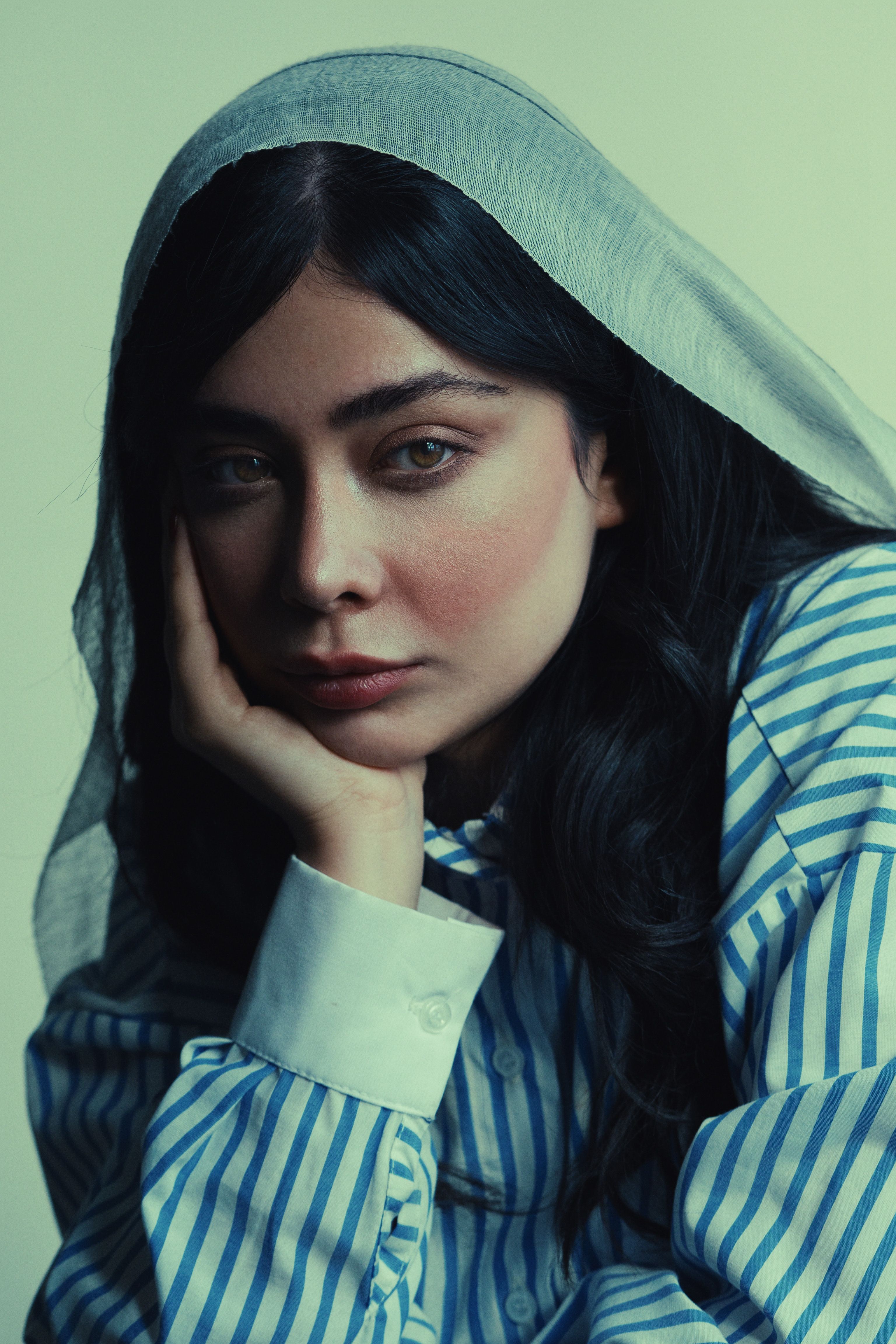 A contemplative woman wearing a striped shirt and headscarf.