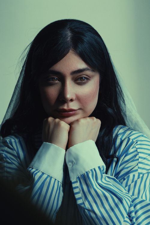 Free A pensive woman in a striped shirt, contemplating with hands under chin. Stock Photo