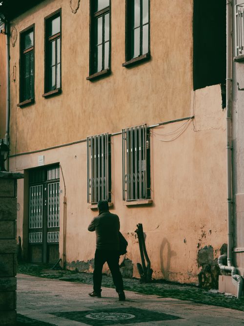 Free A solitary man walks down a deserted street past an old, rustic building. Stock Photo