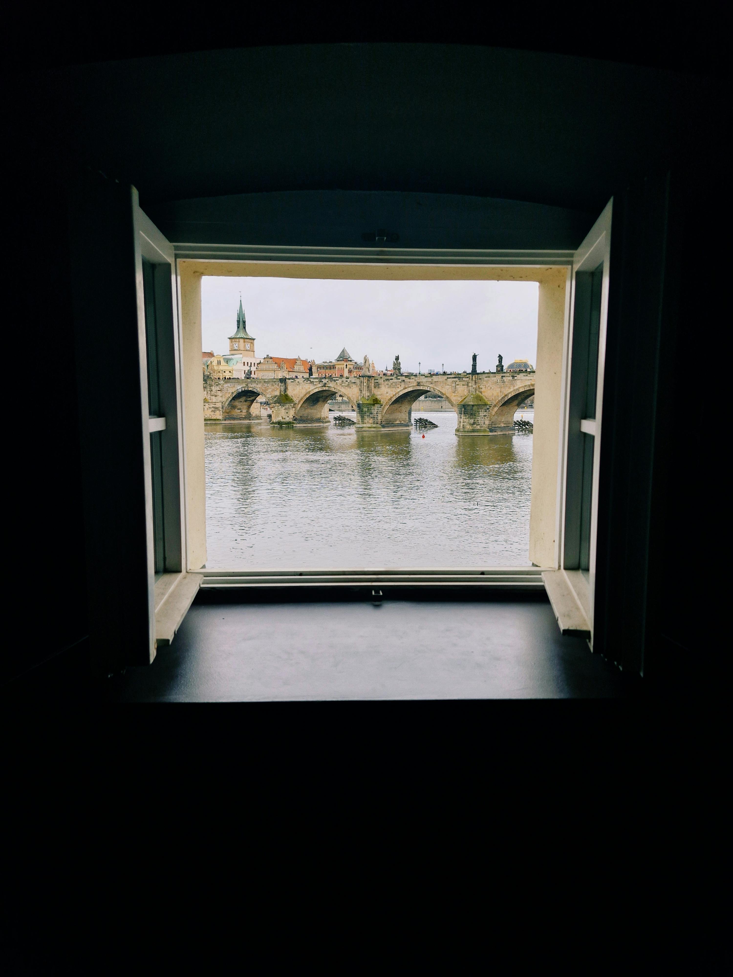 Zadarmo Podmanivý pohľad na Karlov most orámovaný oknom, zachytávajúci podstatu Prahy. Fotka z fotobanky