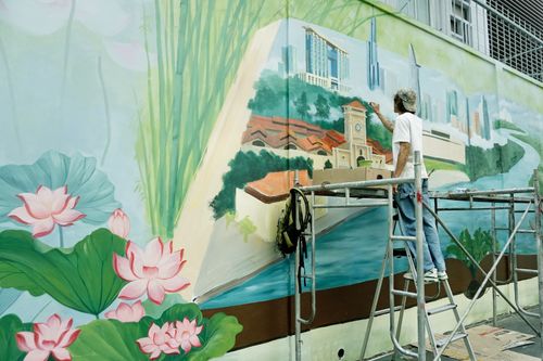 Free An artist paints a detailed urban mural on an outdoor wall, showcasing a cityscape and natural elements. Stock Photo