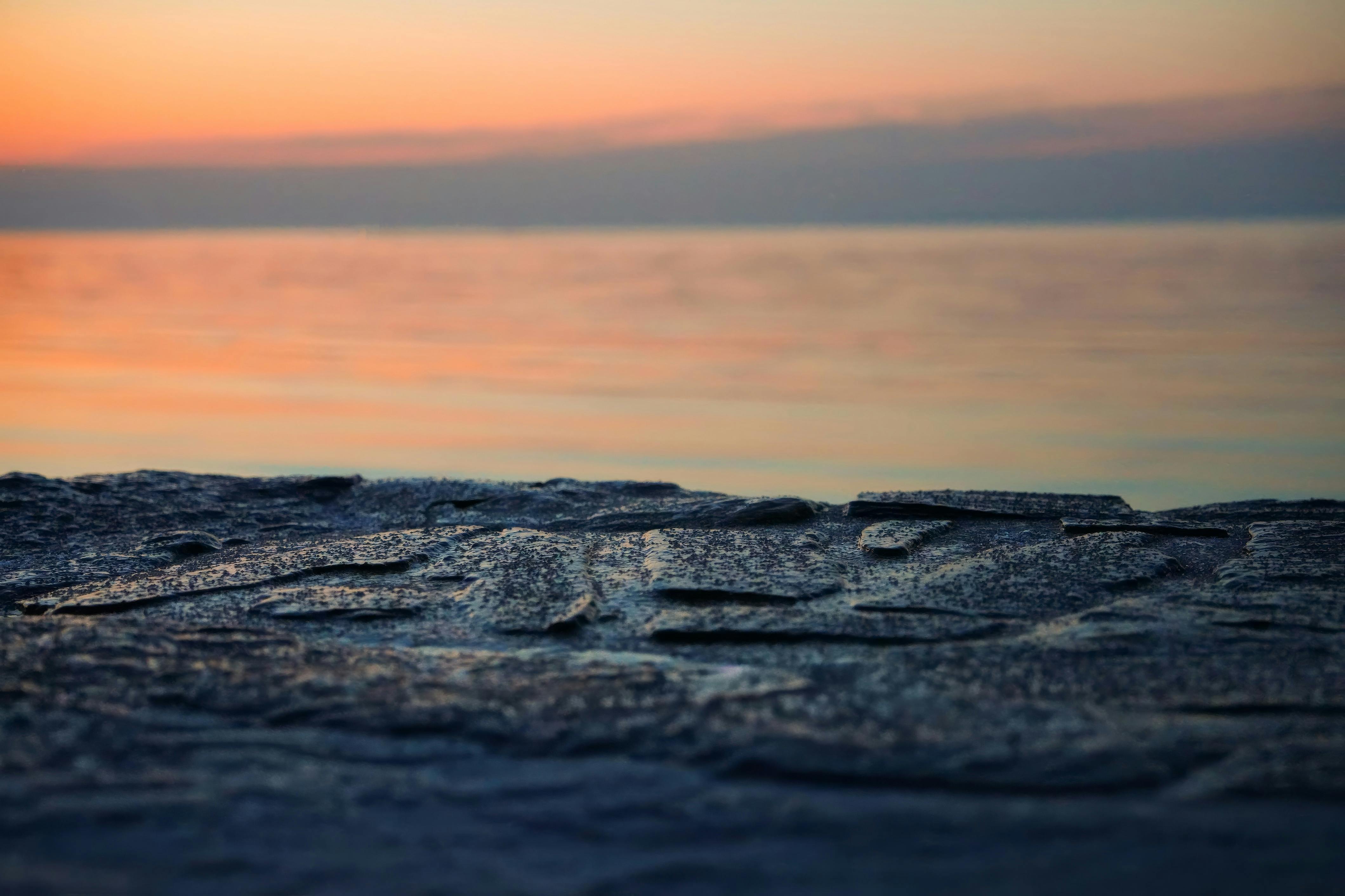 Gratis Un tranquillo tramonto sull'oceano con un primo piano in pietra strutturata, che crea una tranquilla scena costiera. Foto a disposizione