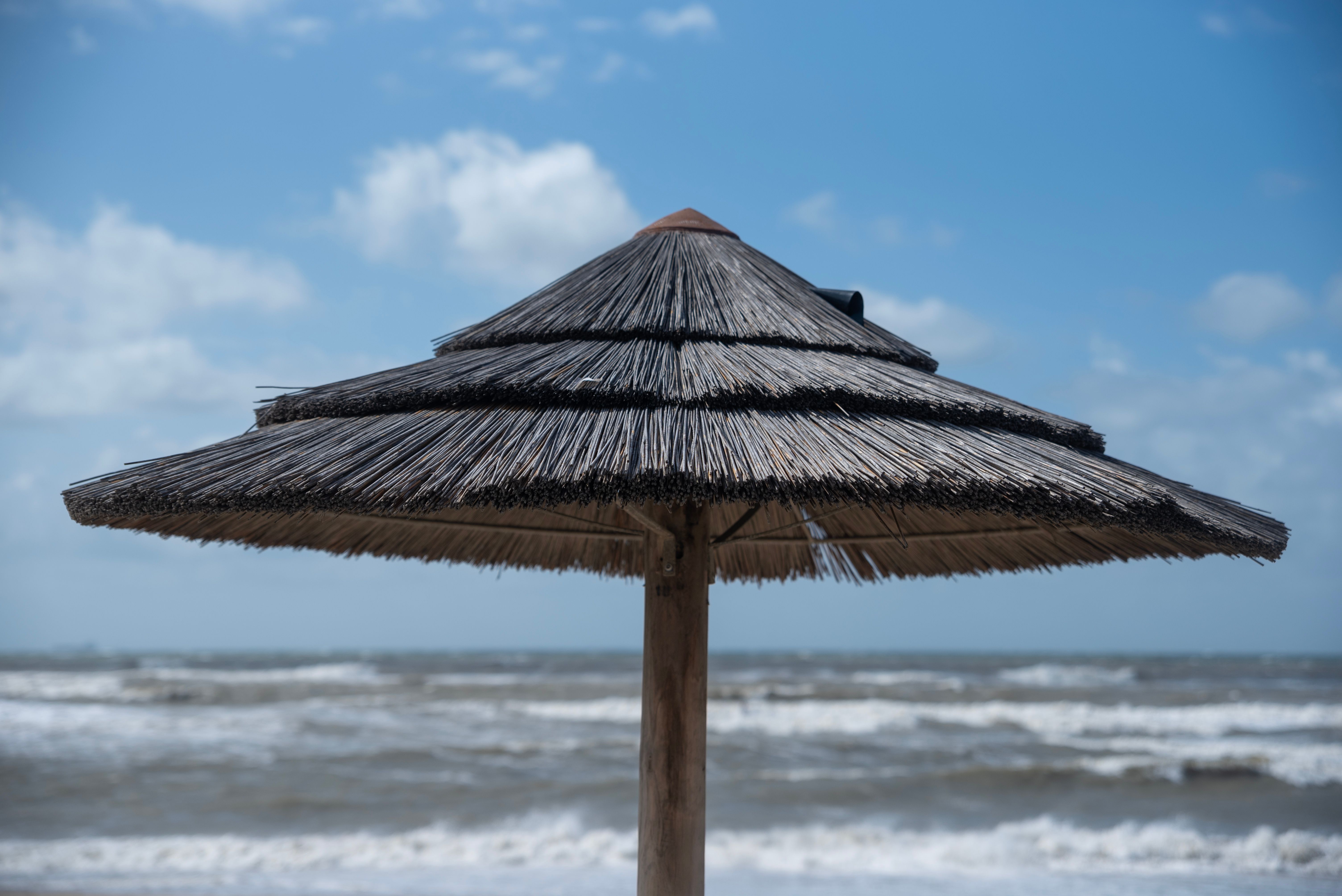 A solitary thatch umbrella overlooking a serene beach scene with calm waves.
