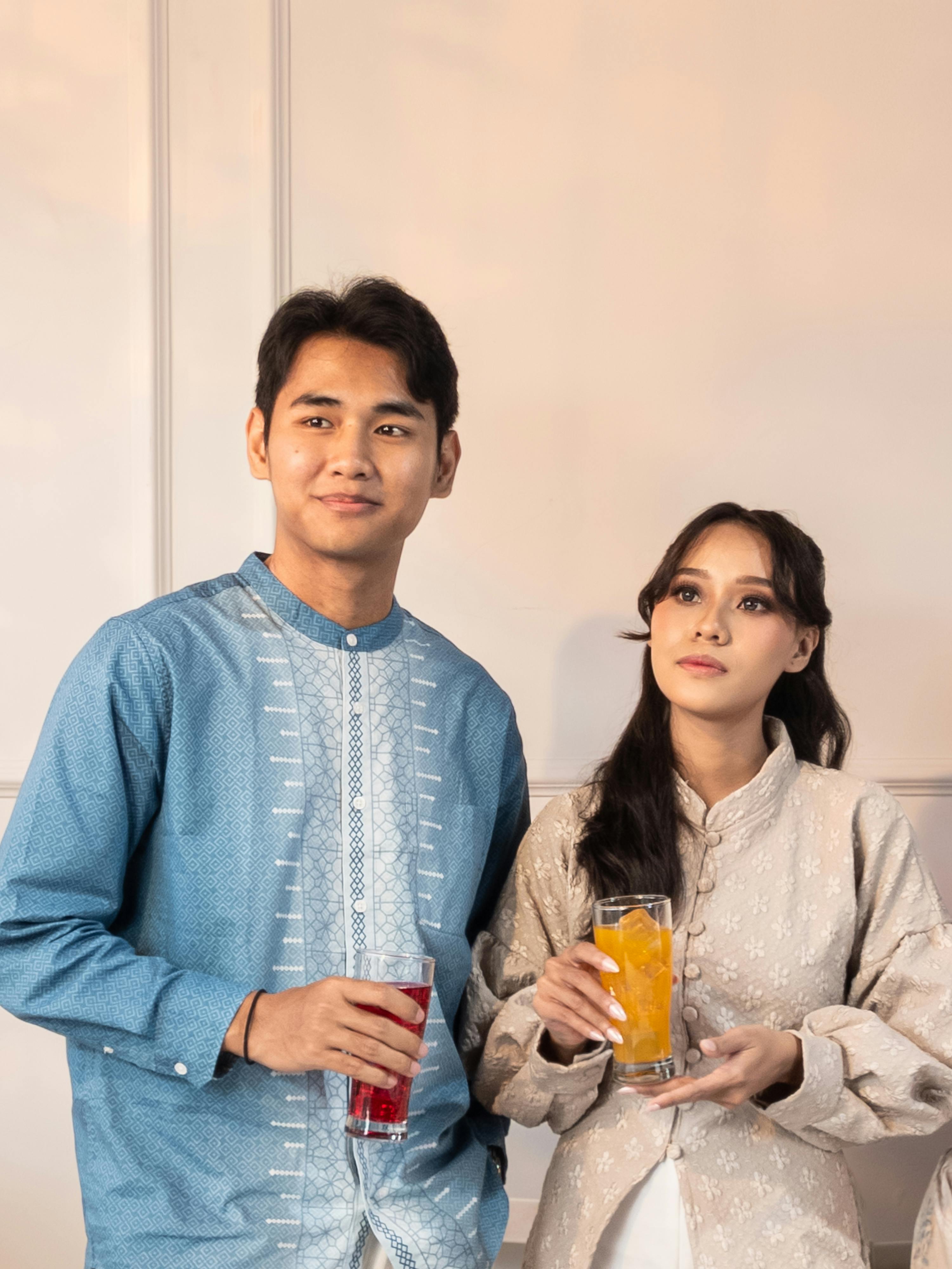 Gratis Una giovane coppia in abiti tradizionali sorseggia un drink in un locale a Giacarta, Indonesia. Foto a disposizione