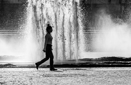 Free Black and white silhouette of a woman walking past a large outdoor water fountain. Stock Photo