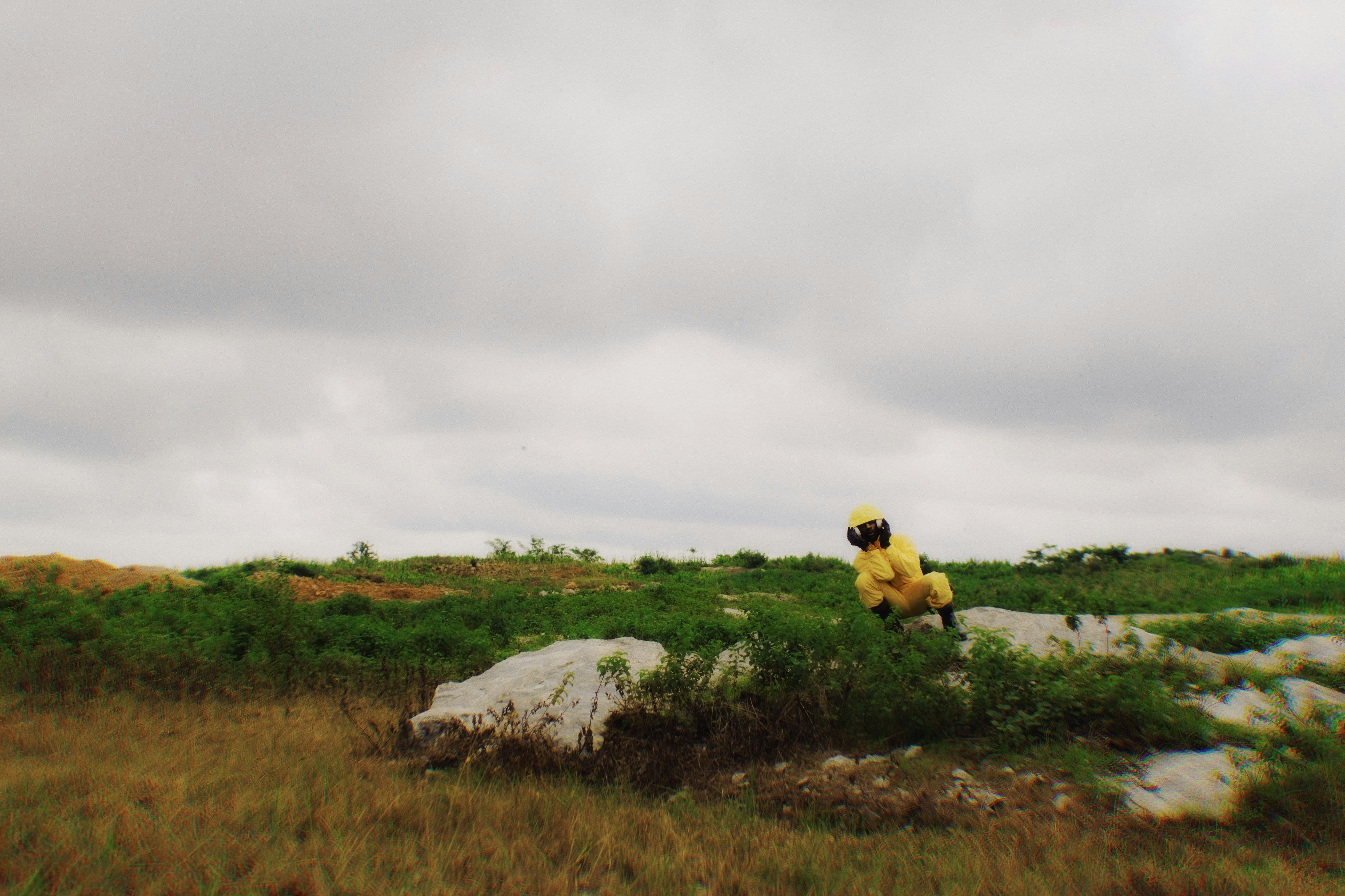 免费 一名身穿黄色防护服的人坐在户外，周围绿树环绕，天空阴云密布。 素材图片