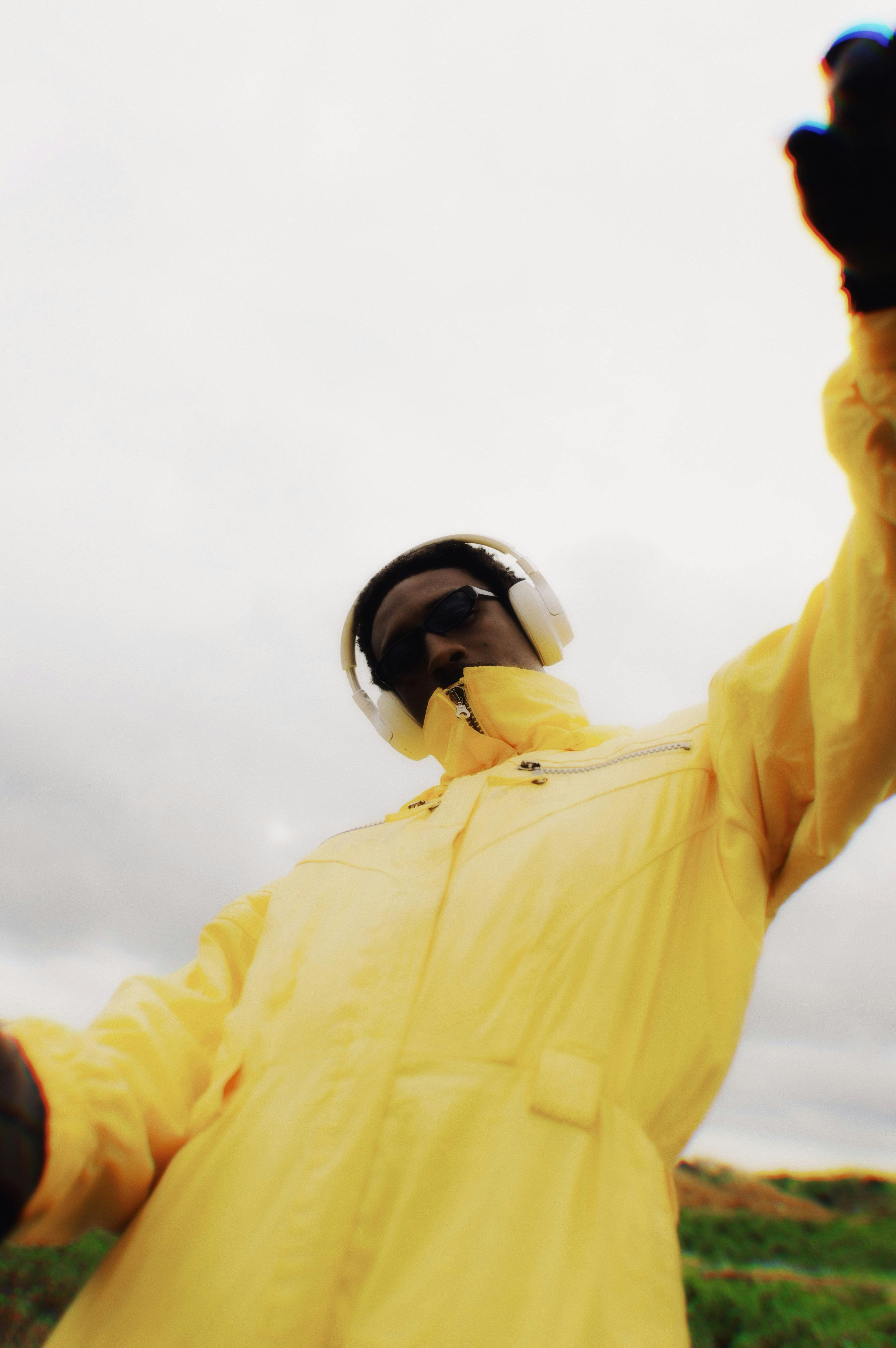 Δωρεάν Ένα εντυπωσιακό καλλιτεχνικό πορτρέτο ενός ενήλικα που φοράει ένα φωτεινό κίτρινο αδιάβροχο με ακουστικά, με φόντο μια εξωτερική αυλή στη Νιγηρία. Φωτογραφία από στοκ φωτογραφιών