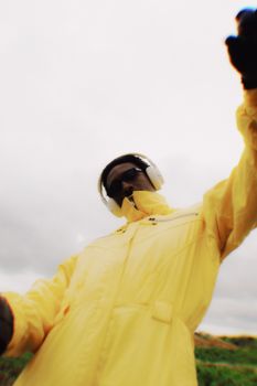A striking artistic portrait of an adult wearing a bright yellow raincoat with headphones, set against an outdoor backdrop in Nigeria.