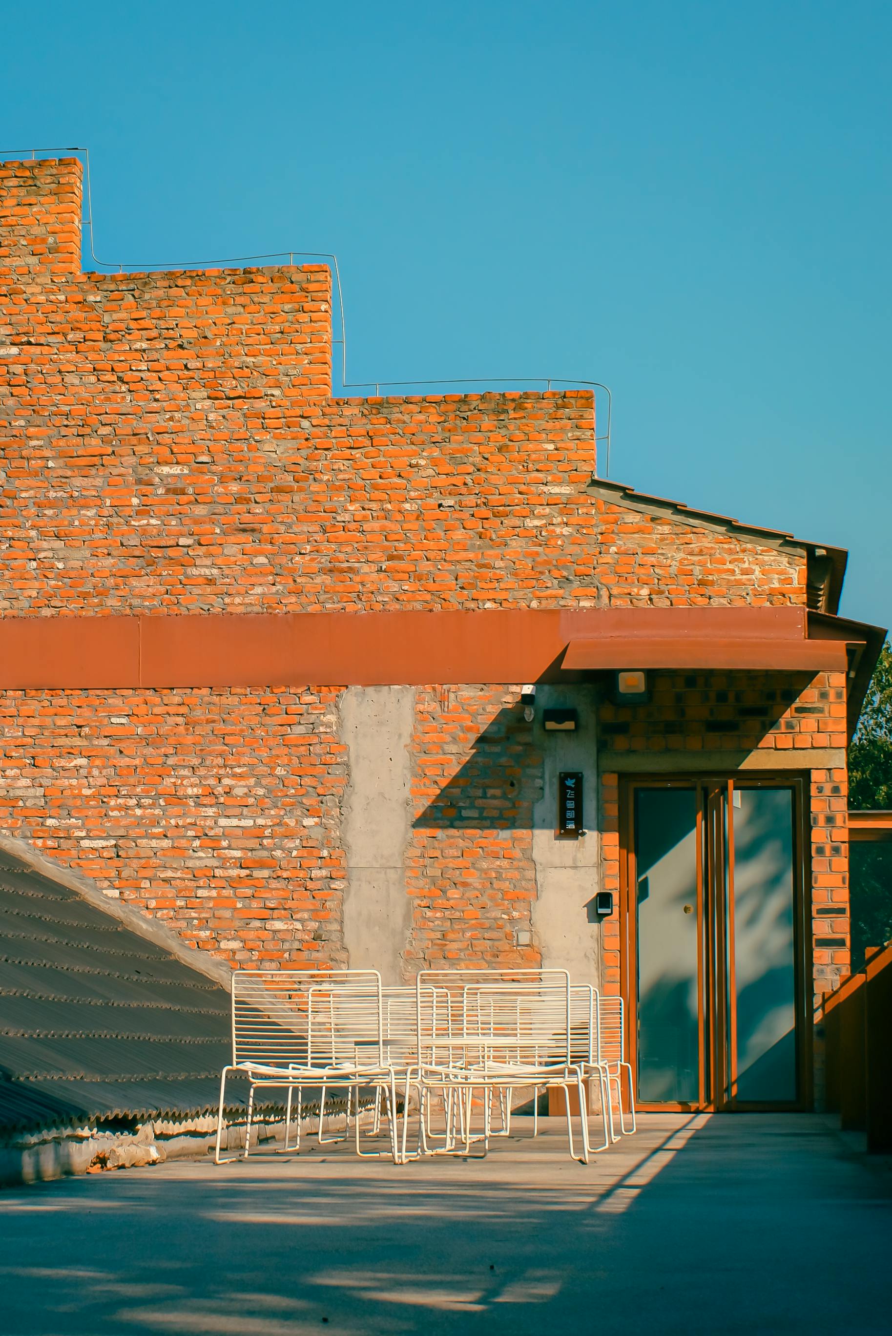 Gratis Tagterrasse med moderne hvide stole mod en rustik murstensvæg under klar blå himmel. Lagerfoto