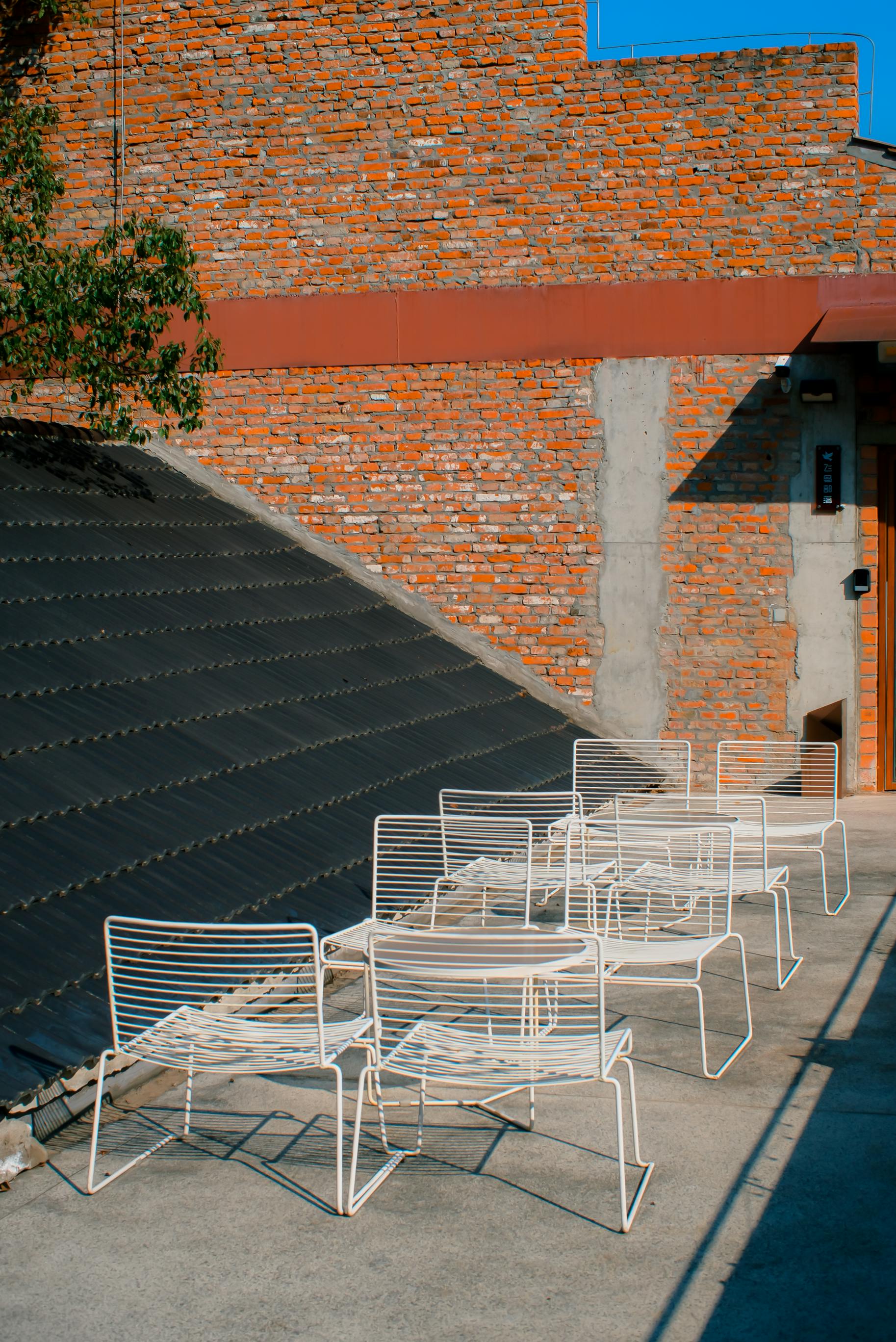 Gratis Elegante patio esterno con sedie in metallo contro un muro di mattoni, in posizione soleggiata. Foto a disposizione