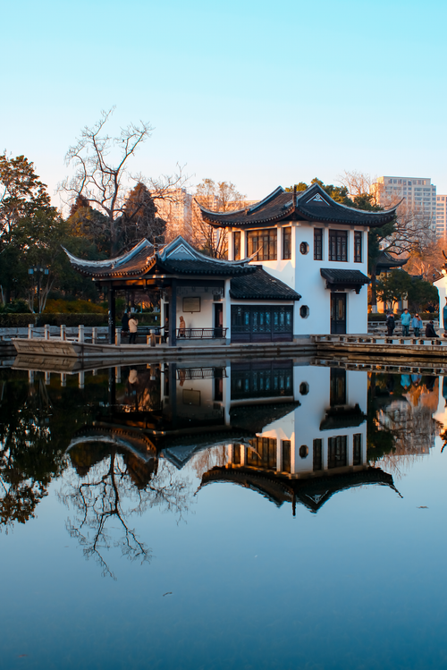 Free Serene scene of a traditional Chinese pavilion reflected in a calm lake at sunset. Stock Photo