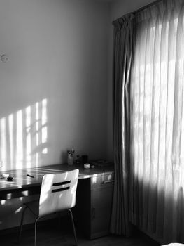 A minimalist black and white home office with a chair and desk illuminated by window light.