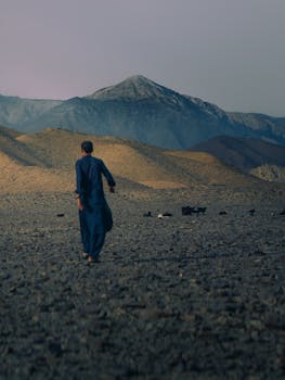 A solitary figure walks across the rocky terrain of Balochistan with mountains in the background.