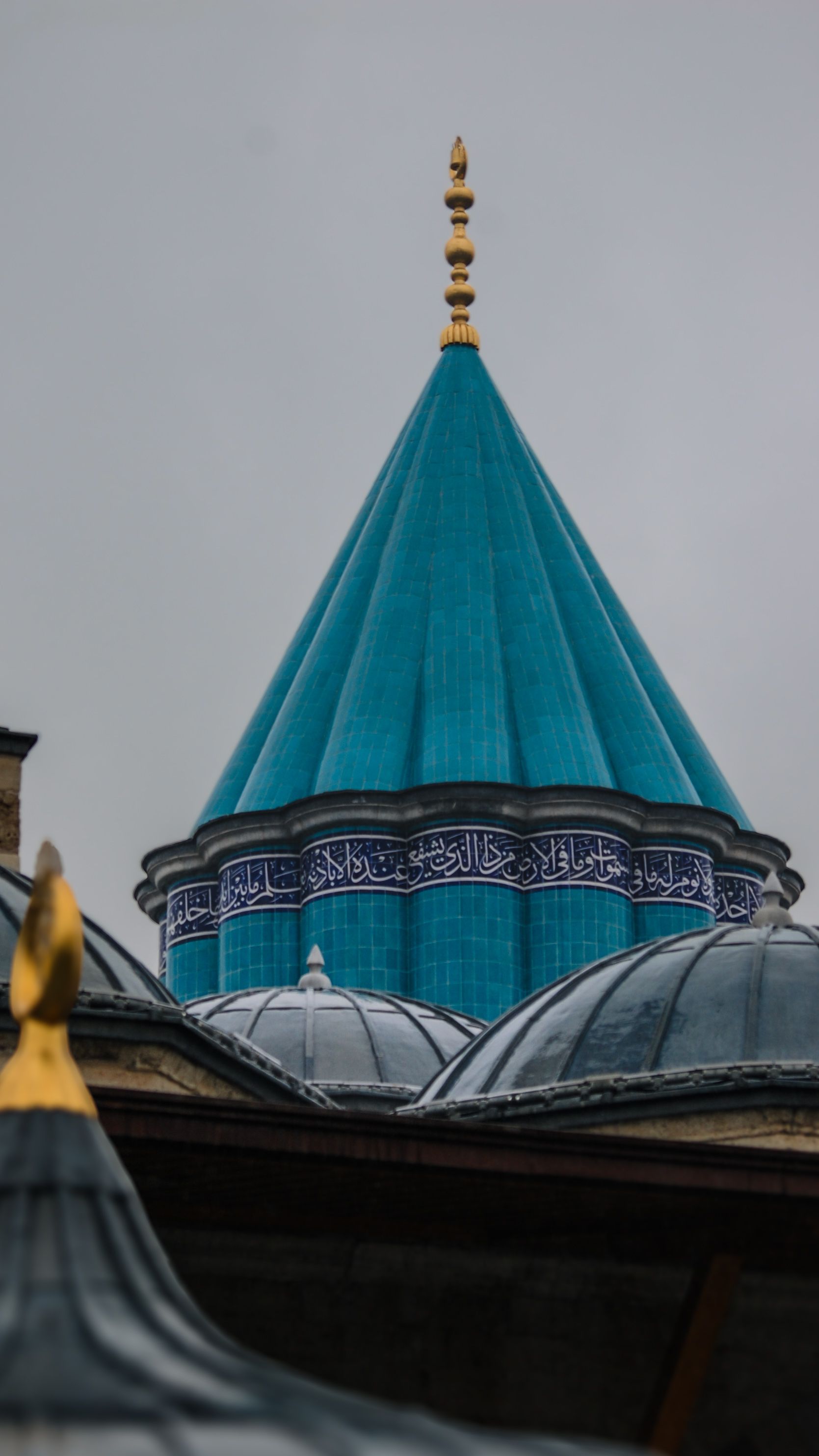The striking green tile dome of the Mevlana Museum in Konya, Türkiye, under a cloudy sky.