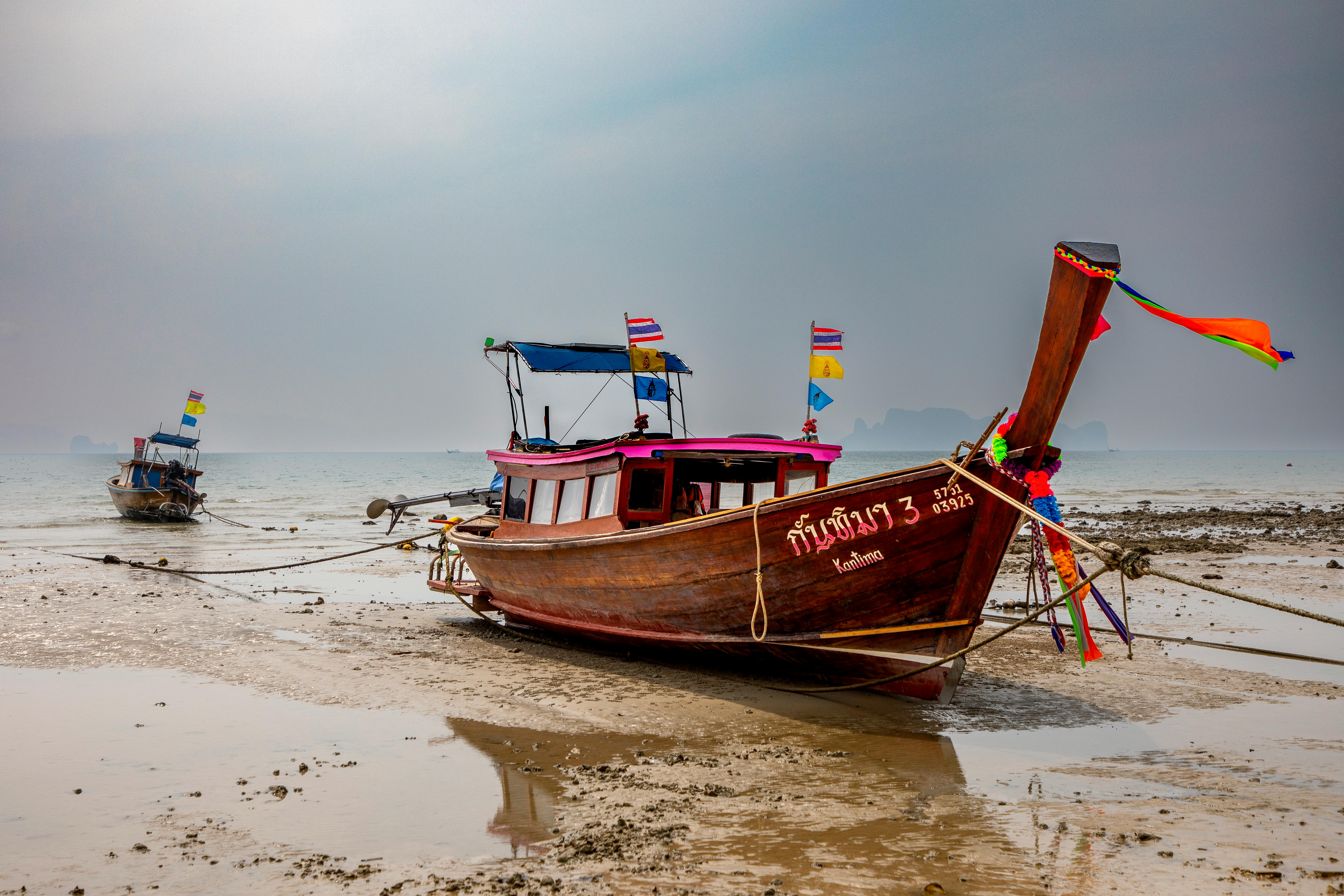 Traditional Thai longtail boats anchored on Krabi Beach, Thailand with vibrant flags and tranquil waters.