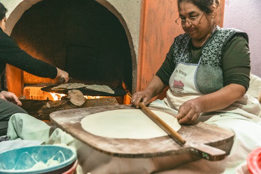 Woman rolling dough for traditional bread by a wood-fired oven in Türkiye.