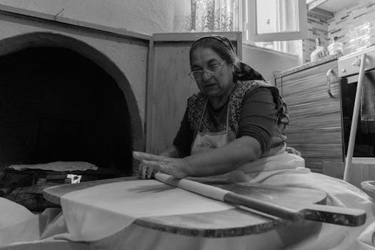 A Turkish woman skillfully prepares flatbread in her home kitchen with a wood-fired oven.