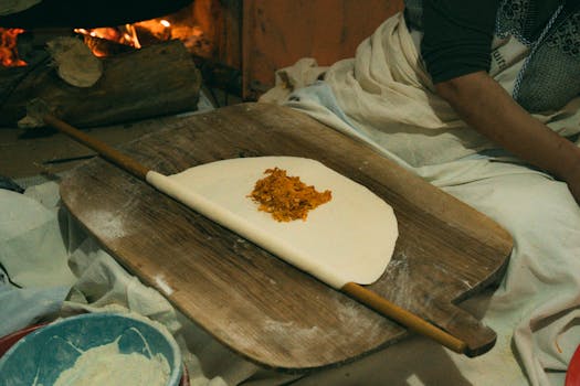 A woman preparing traditional Turkish flatbread with filling by a cozy fire.