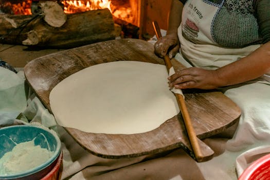Woman preparing dough in Türkiye with a wooden rolling pin by a warm fire.