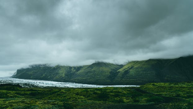 多云天空下，青山郁郁葱葱，景色宁静，还能瞥见冰川