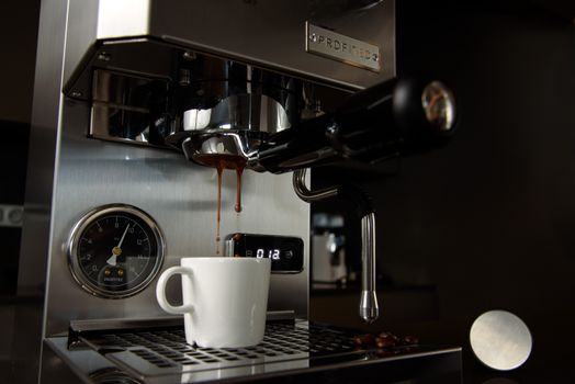 Close-up of espresso brewing into a cup using a professional espresso machine in low light.