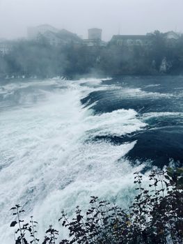 Dramatic waterfall flowing under mist with distant buildings visible.