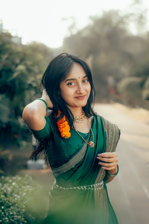Free Portrait of an elegant young woman in a green saree with floral jewelry, set in a lush outdoor environment. Stock Photo