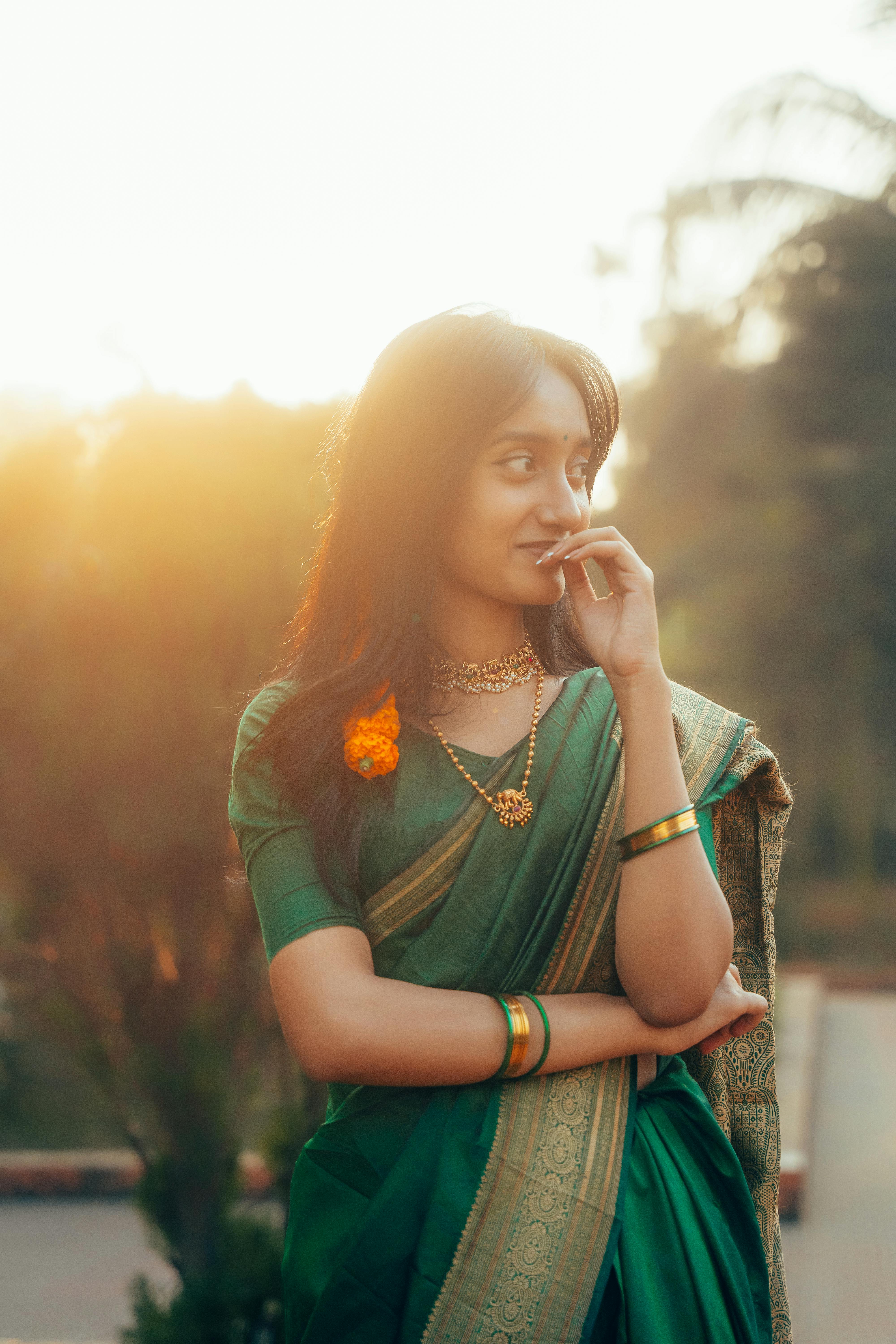 ฟรี ภาพถ่ายอันสงบเงียบของหญิงสาวในชุดสาหรีสีเขียว ถ่ายได้อย่างงดงามในยามพระอาทิตย์ตกดิน สะท้อนความสง่างามและความงดงามทางวัฒนธรรม คลังภาพถ่าย