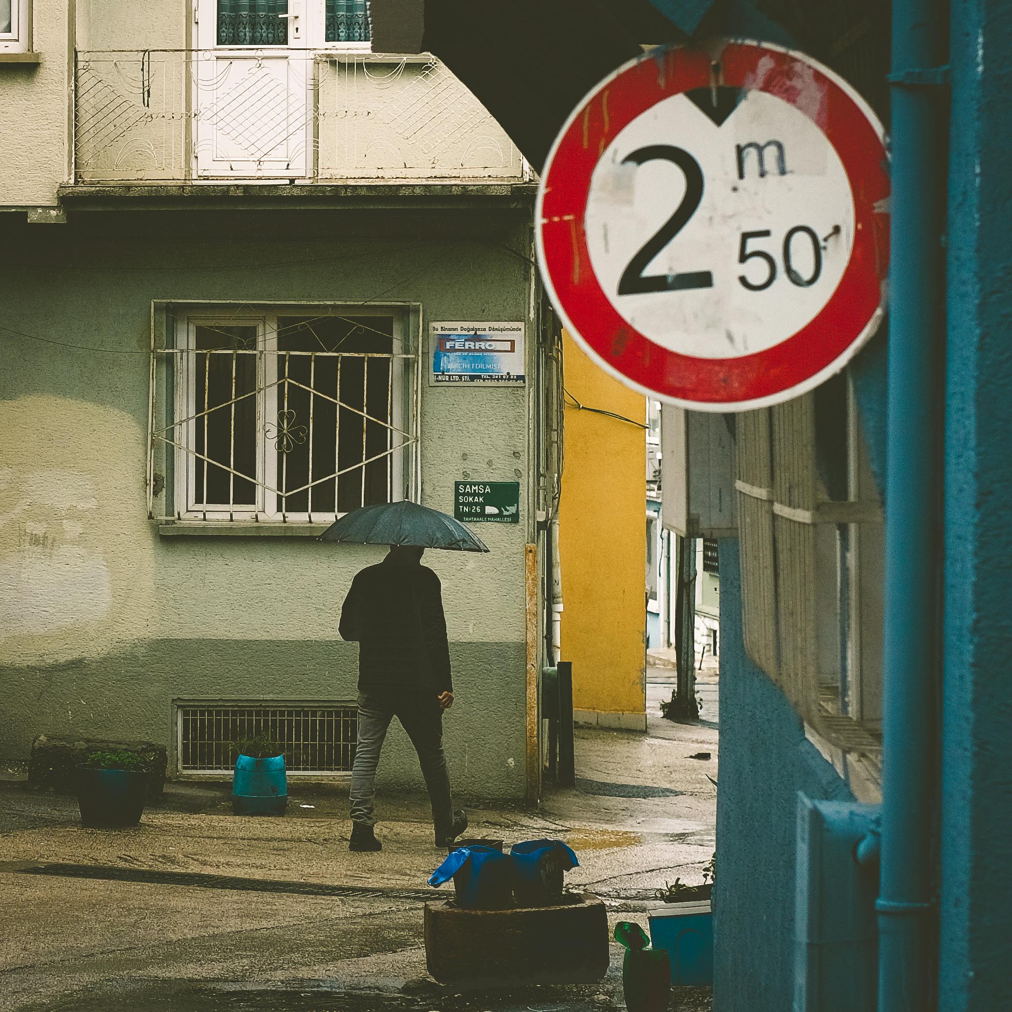 ingyenes Városi utcakép, ahol egy esernyőt tartó személy elsétál egy magasságkorlátozást jelző tábla mellett. Stockfotó