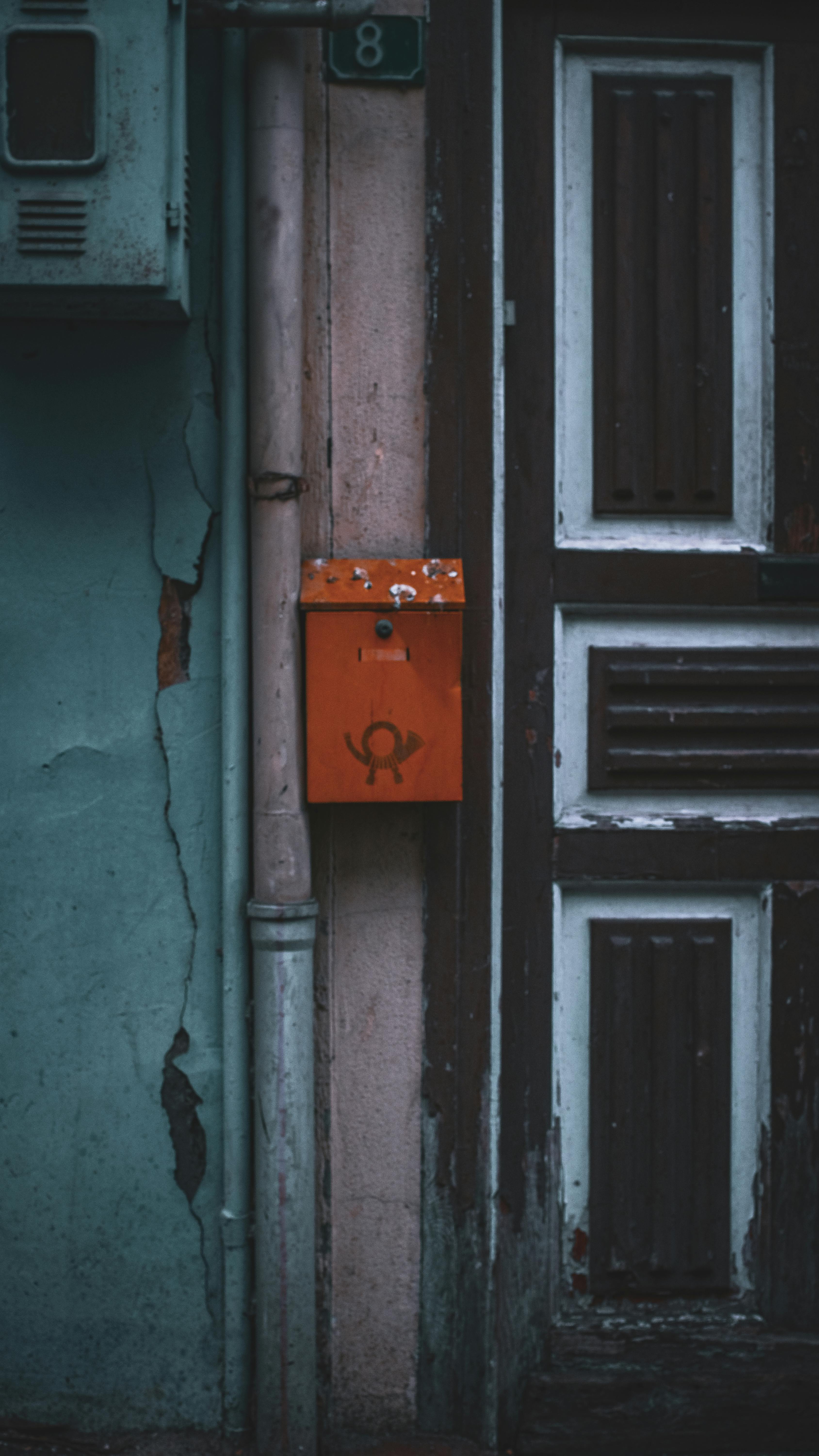 Gratis Un buzón vintage de color naranja montado sobre una puerta rústica desgastada con pintura desconchada, que enfatiza una estética de decadencia urbana. Foto de stock