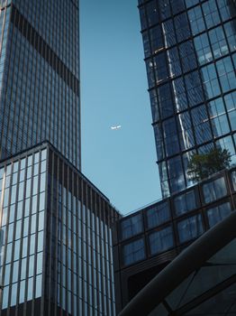 Airplane seen between modern skyscrapers in New York City with clear blue sky.