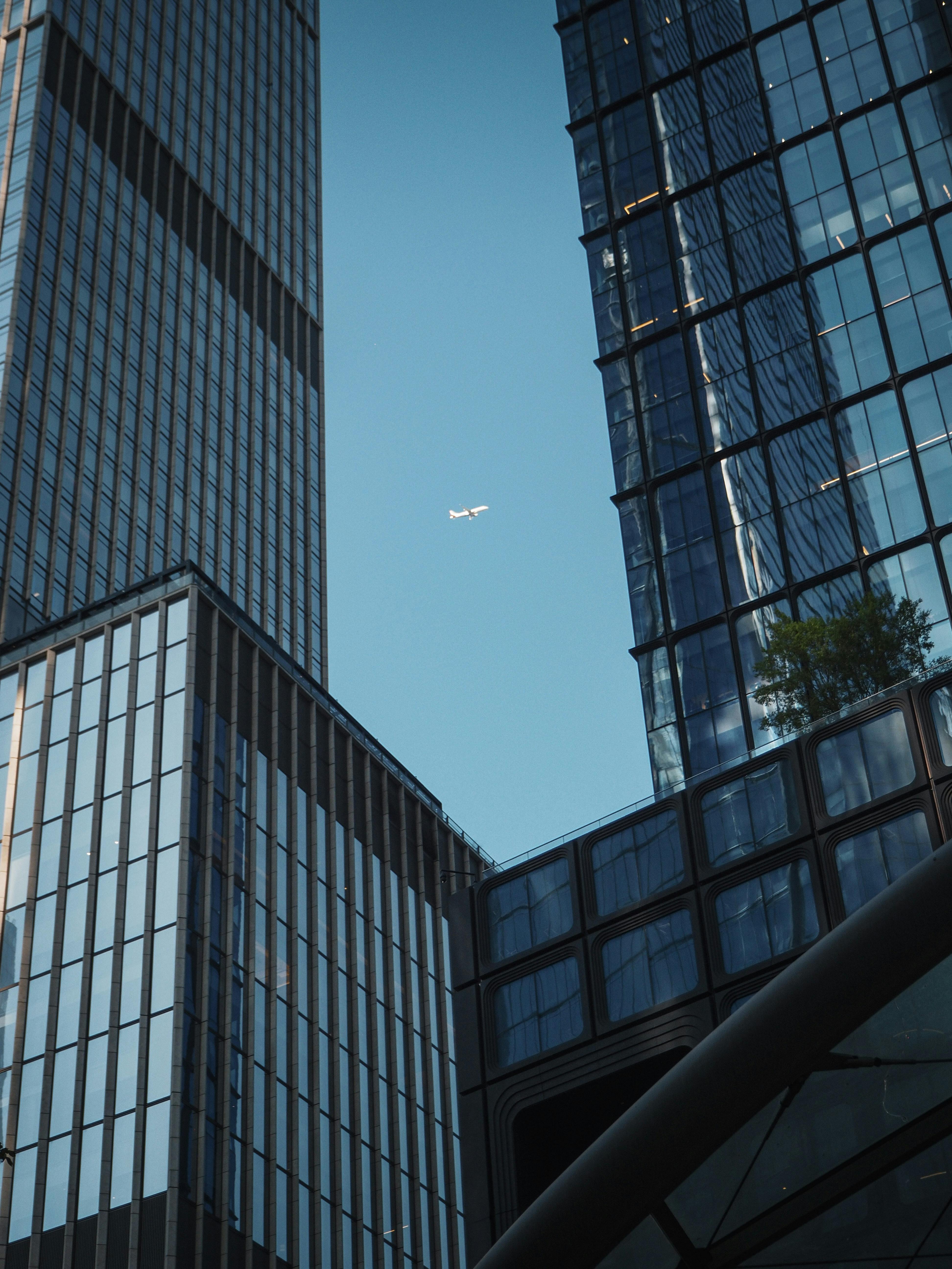 gratis Een vliegtuig gezien tussen moderne wolkenkrabbers in New York City, met een helderblauwe lucht. Stockfoto