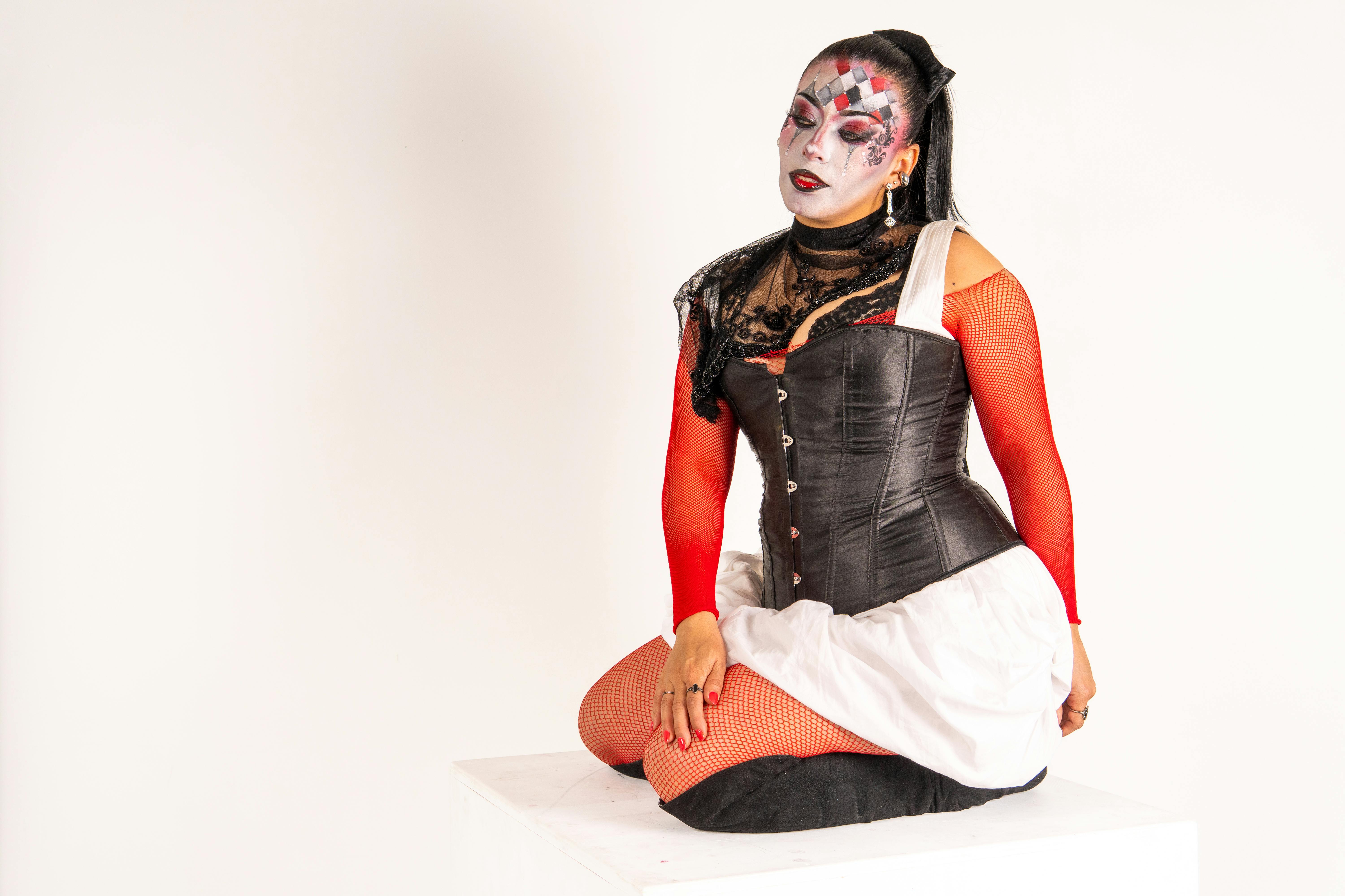 무료 할리퀸풍의 화장과 의상을 입은 여성이 단상 위에 앉아 있는 모습의 초상화. 스톡 사진