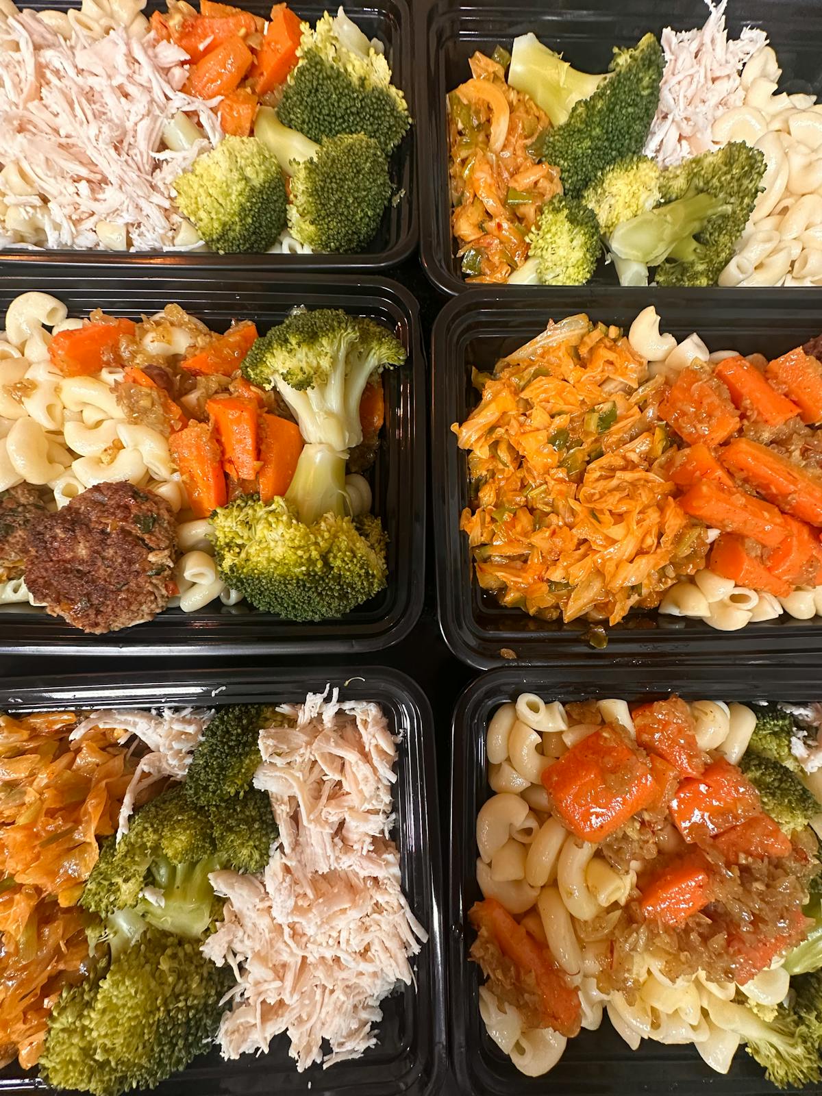Colorful meal prep trays with pasta, broccoli, chicken, and carrots