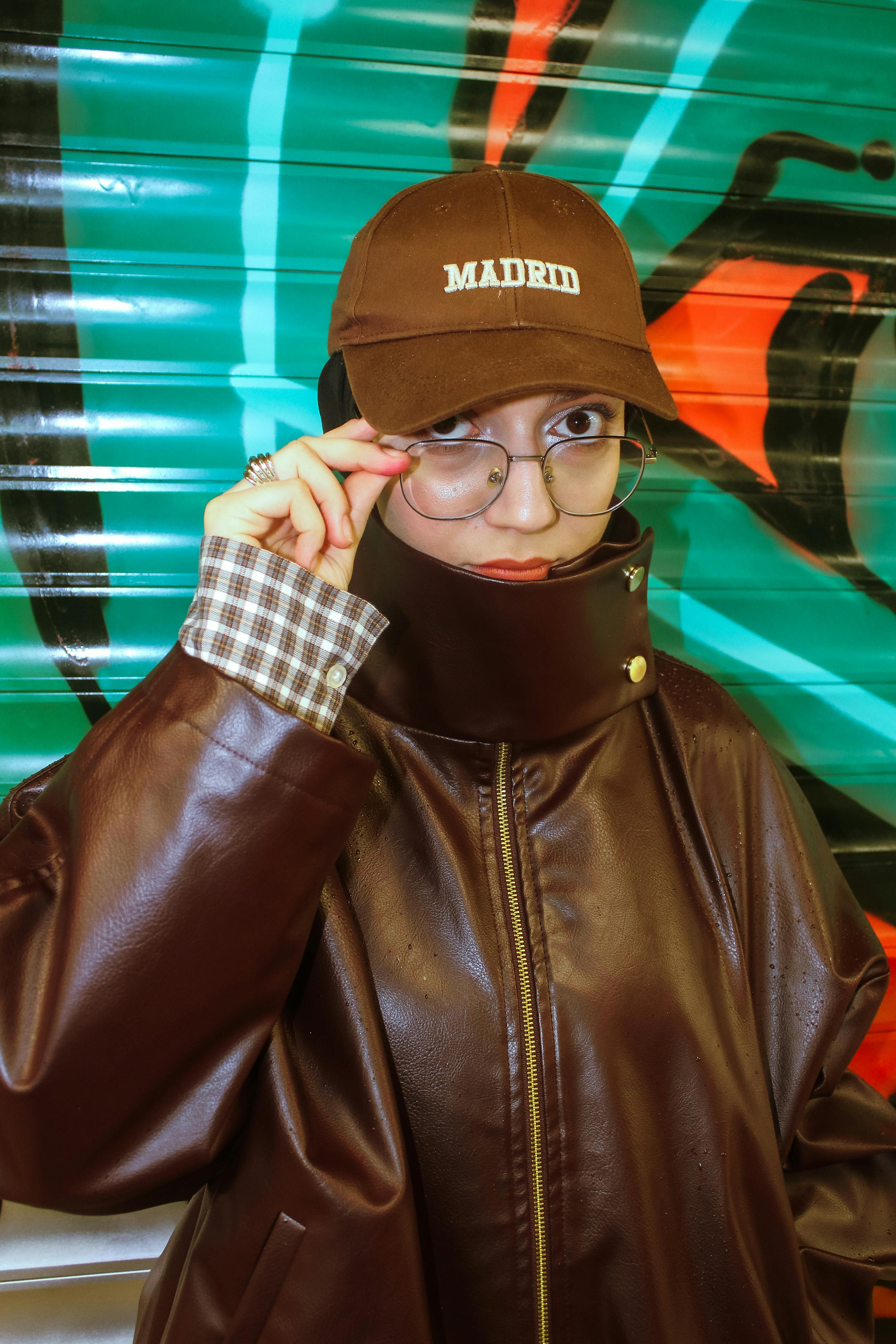 Miễn phí Một cá nhân sành điệu trong trang phục da và đội mũ, phía sau là dòng chữ 'MADRID' trên nền graffiti sống động. Ảnh lưu trữ