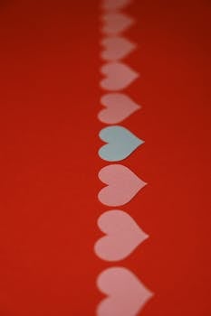 A creative arrangement of paper hearts on a vibrant red background, symbolizing love and romance.