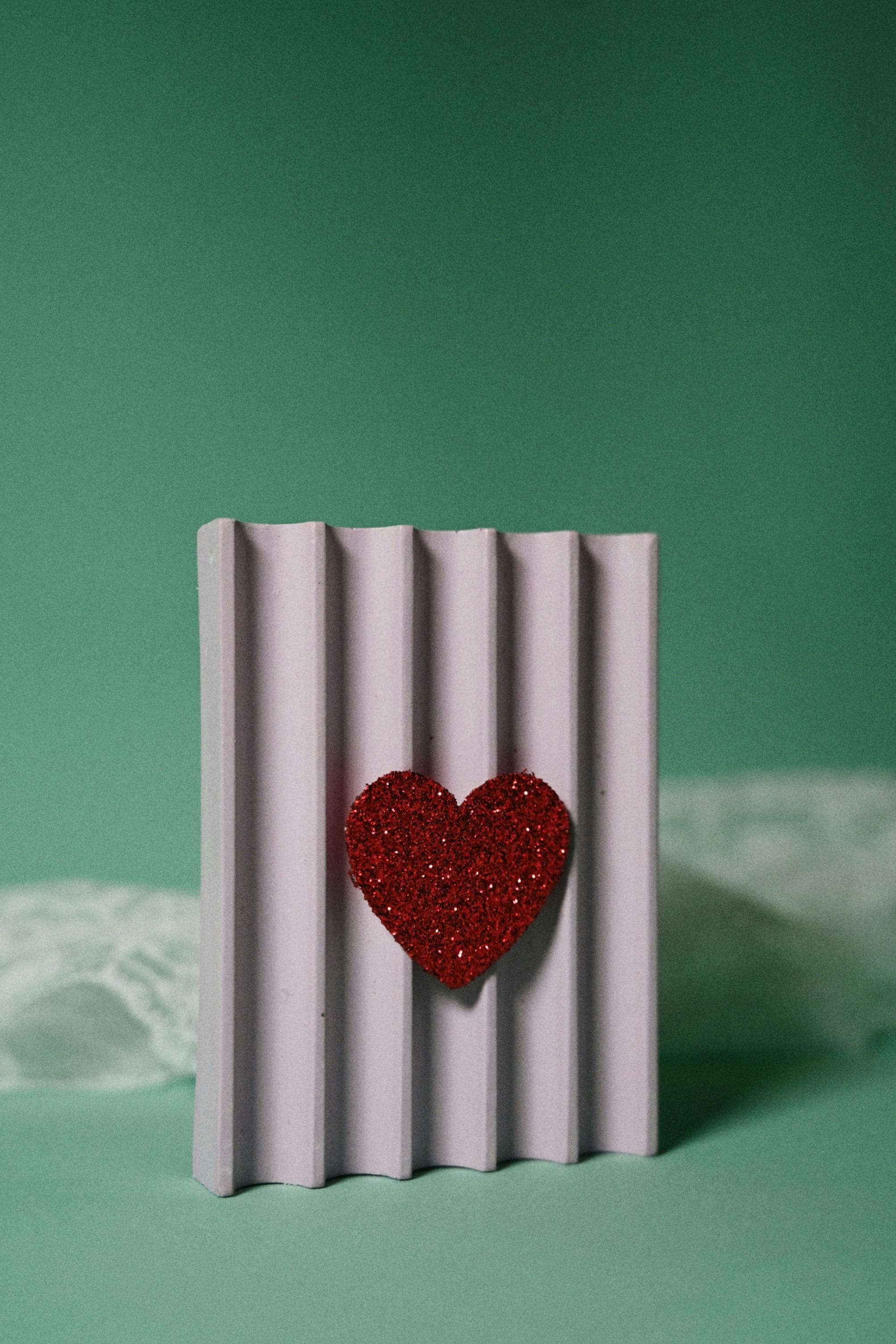 Free A glittering red heart on a textured purple surface against a green backdrop, perfect for Valentine themes. Stock Photo