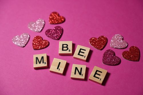 Free A romantic Valentine's Day theme with wooden tiles spelling 'Be Mine' surrounded by glittery hearts. Stock Photo