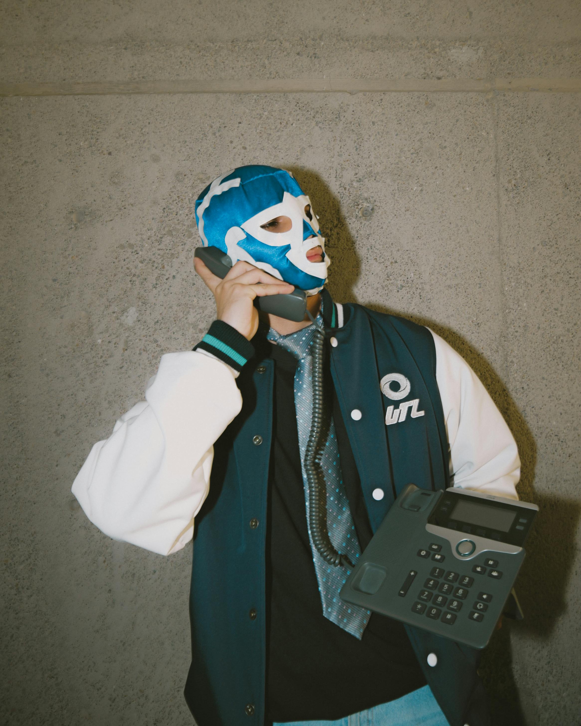 Free A person in a lucha libre mask poses with a retro telephone, showcasing unique style. Stock Photo