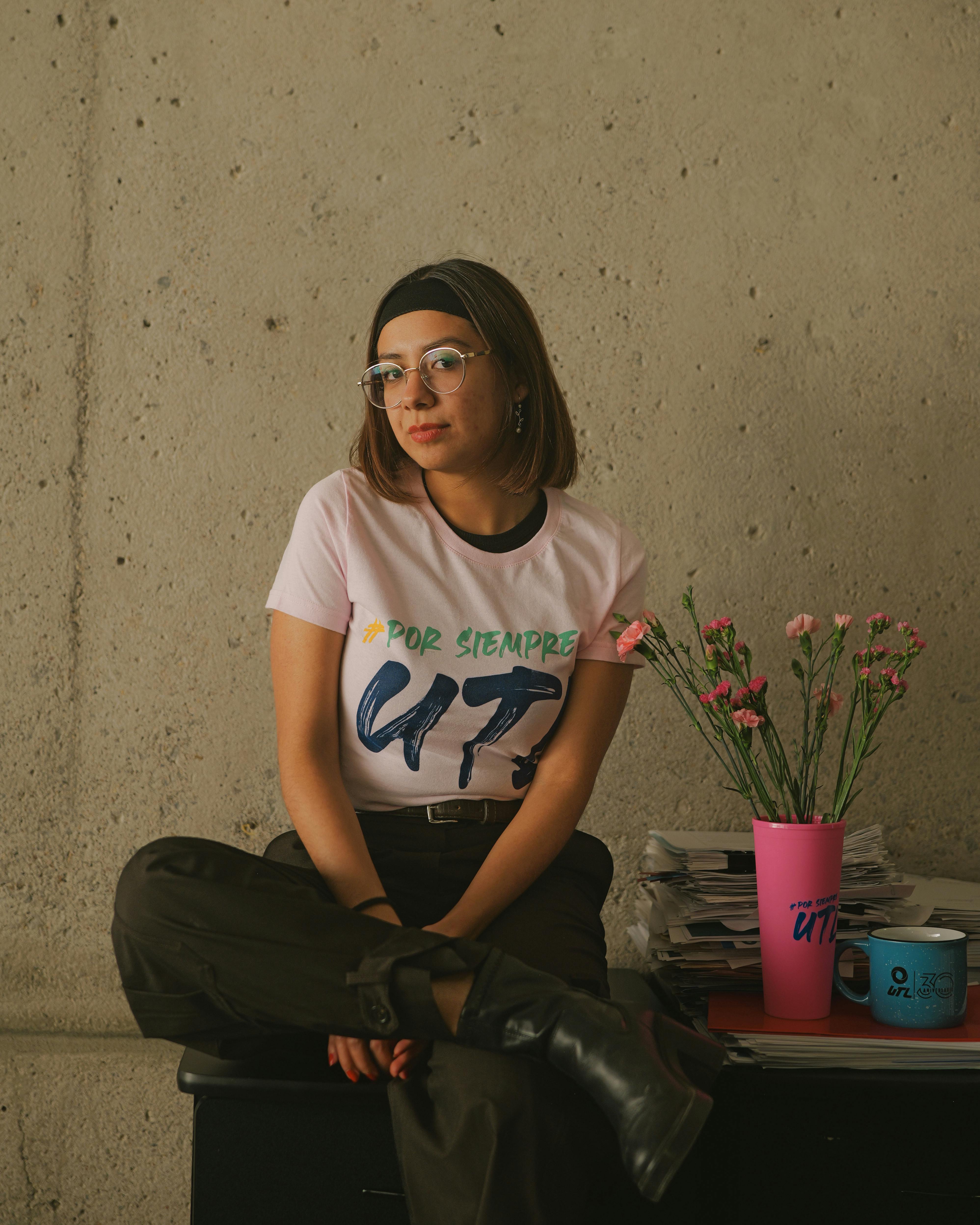 Gratis Ritratto informale di una giovane donna in un interno con un vaso di fiori rosa, che trasmette un'atmosfera rilassata e composta. Foto a disposizione