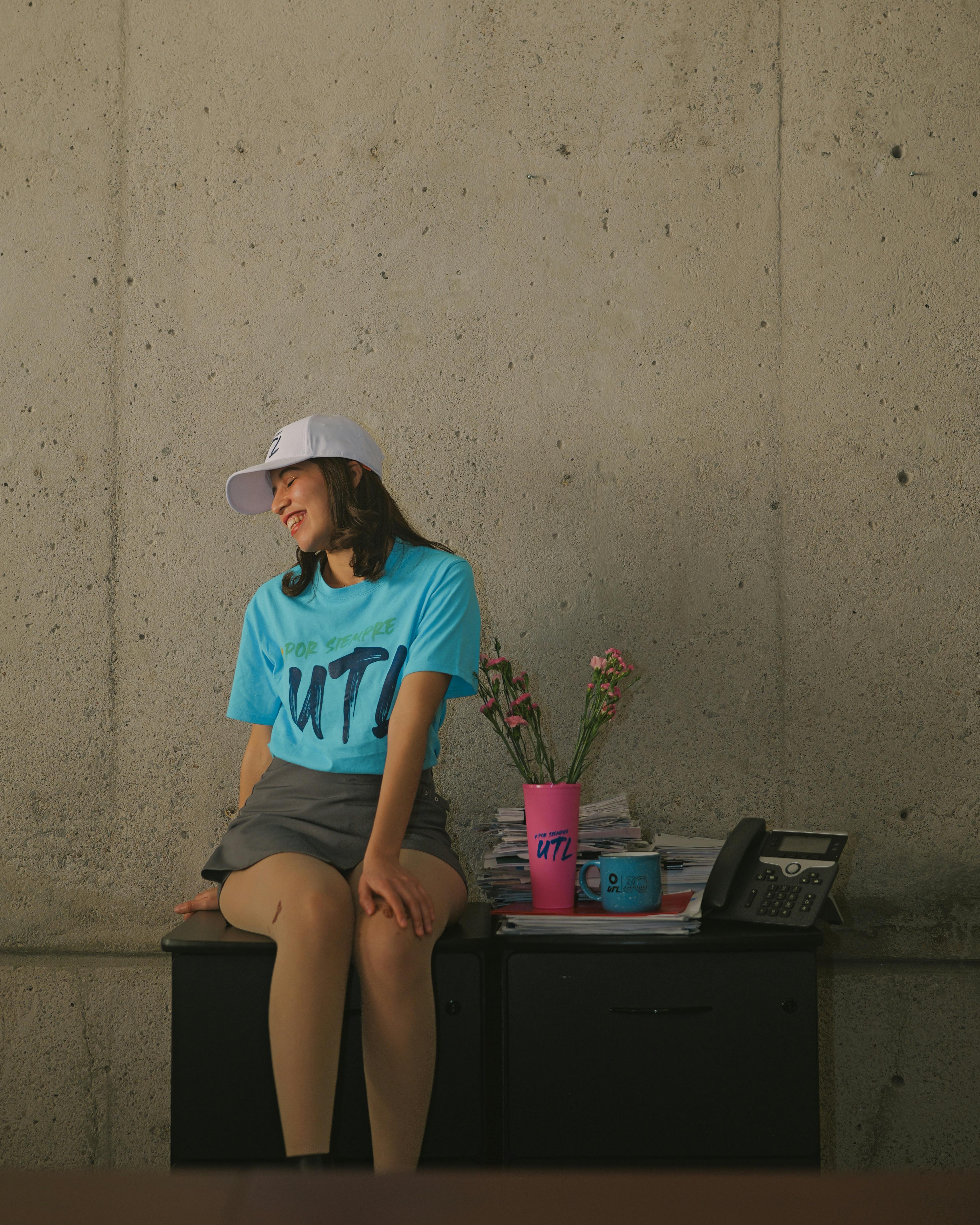 gratis Jonge vrouw zit binnen aan een bureau, casual gekleed, met een telefoon en mokken om zich heen. Stockfoto